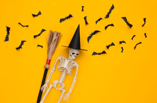 Skelet in een heksenhoed en bezemsteel, vliegende vleermuizen op gele achtergrond. Halloween handgemaakte inrichting. Bovenaanzicht. plat leggen