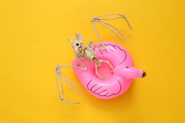 Skeleton bat in inflatable flamingo on blue background Halloween party Concept art Creative layout Minimalism