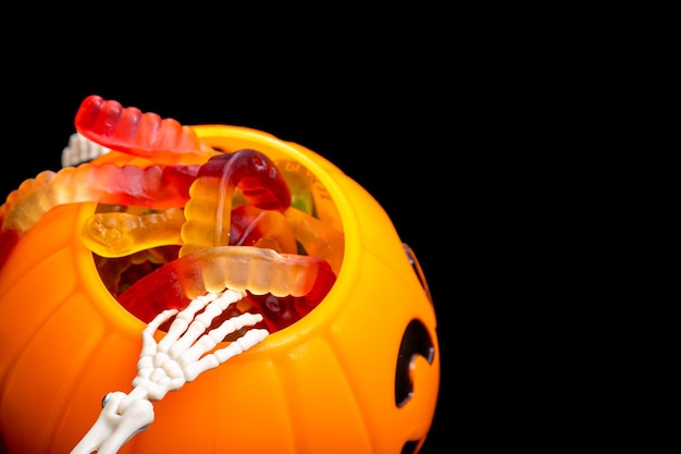 Le mani dello scheletro estraggono i vermi della marmellata da un secchio a forma di caramella di zucca su sfondo nero