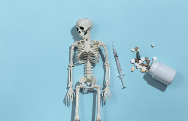 Skeleton and syringe, pills bottle on a blue bright background. Drug addiction. 