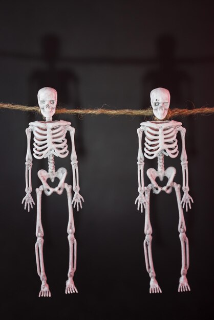 Skeletons hang on a rope on a black background with red illumination. Happy Halloween holiday.