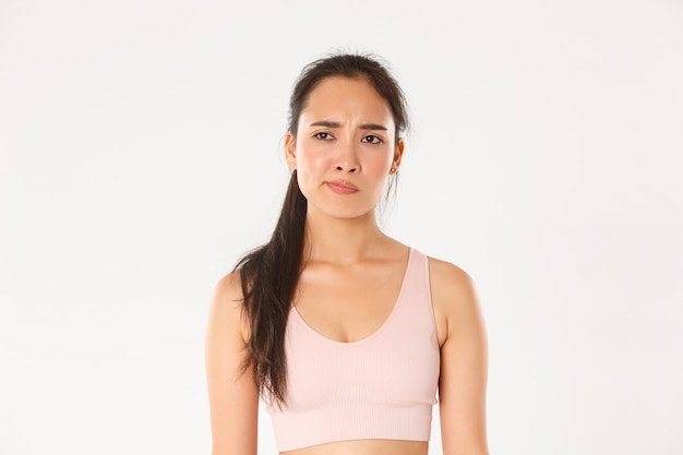 Skeptical and displeased asian sportswoman, female athlete smirk disappointed and unamused, looking left with frowning face, white background.