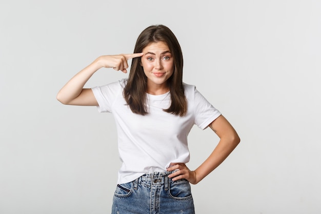 Skeptical and displeased brunette girl pointing at head, scolding someone being crazy.