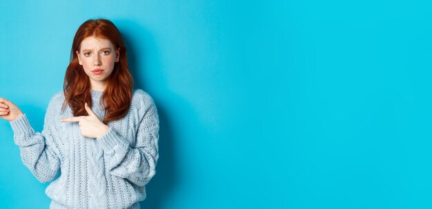 Skeptical and displeased redhead girl pointing fingers left with upset face standing disappointed ag