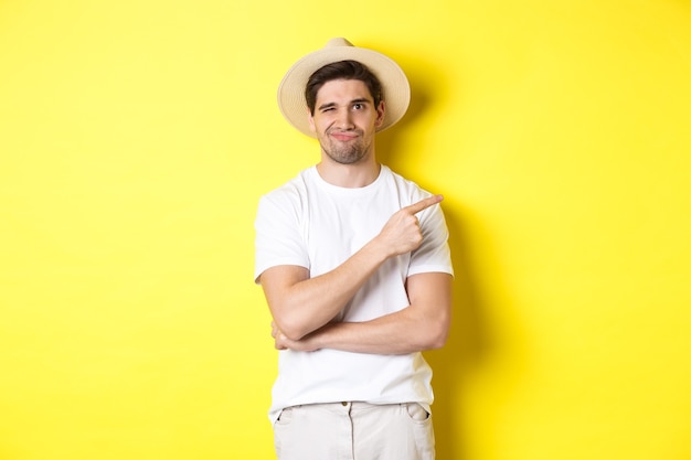 Skeptical male tourist complaining, pointing finger right at something bad or lame, standing unamused against yellow background