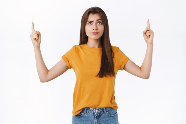 Skeptical, unsure good-looking brunette woman smirk with dismay or scorn, frowning suspicious, pointing and looking with disbelief at strange hideous event, standing white background