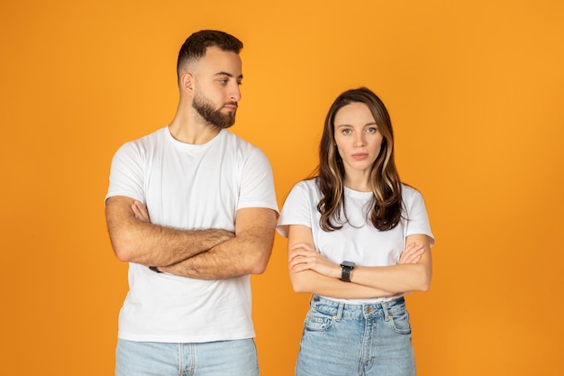 A skeptical young man and woman stand with arms crossed looking at each other