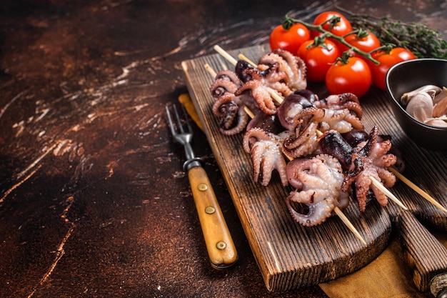 Skewers with bbq roasted baby octopuses Dark background Top view Copy space