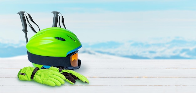 Фото Лыжное снаряжение на белом деревянном столе шлем, перчатки, очки и палки скопируйте пространство рядом со снежными горными вершинами на заднем плане