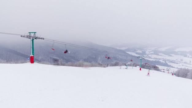 눈 덮인 산과 산 빙하를 배경으로 한 스키 리프트 체어리프트에서 빈 싱글 의자가 위아래로 움직입니다. 스키어 스노 보더와 관광객이 주말에 관광을 왔습니다.