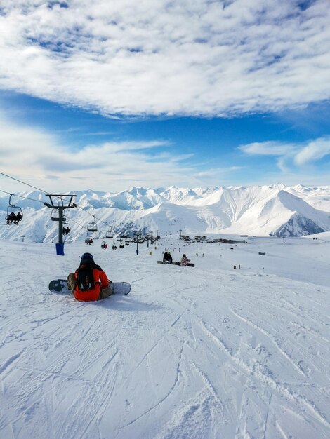 Photo ski resort snowboarder sits on snow view from back snowcapped mountain sunny day active winter spors