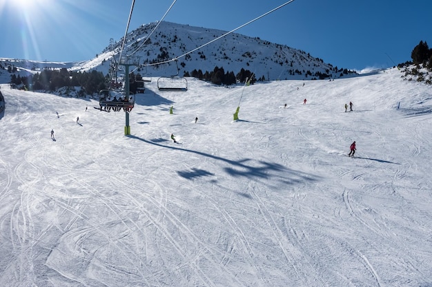 Горнолыжный склон с лыжниками, скользящими по склону в Пиренеях Андорра фото с копирайтом