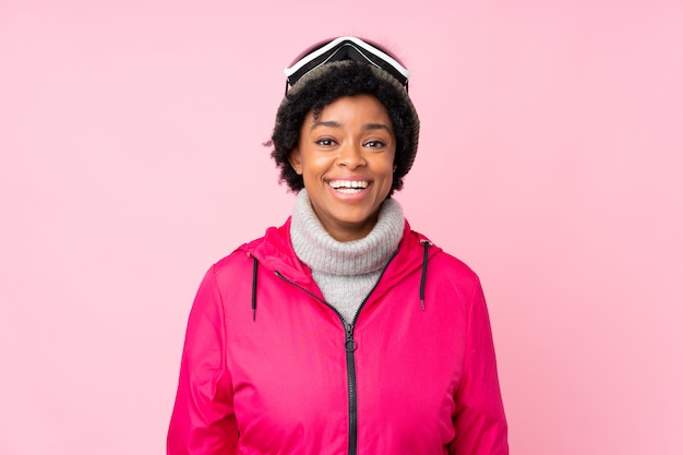 Donna afroamericana dello sciatore con i vetri di snowboard sopra la parete rosa isolata