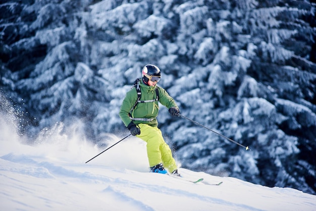 Photo skier backpacker skiing down on slope, raising blizzard snow powder. picturesque forest scenery on blurred background.