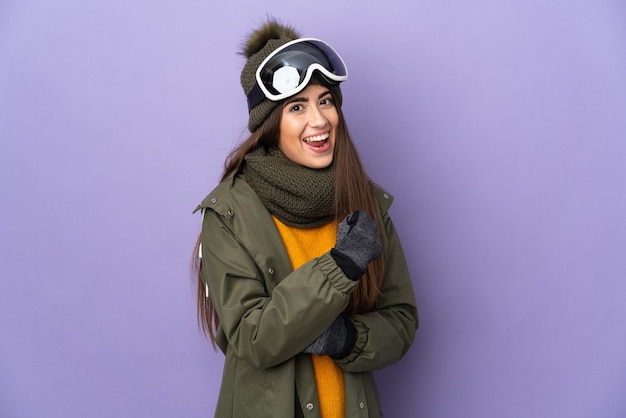 Кавказская девушка лыжника в очках для сноуборда, изолированные на фиолетовом фоне, празднует победу