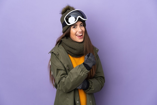 Ragazza caucasica sciatore con occhiali da snowboard isolato su sfondo viola che celebra una vittoria