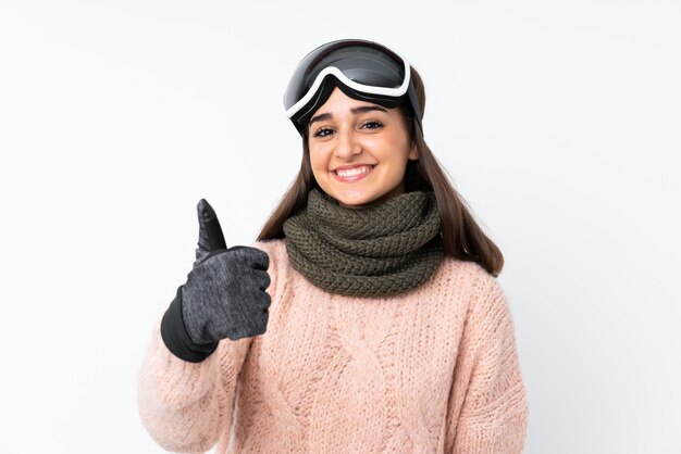 Skier girl with snowboarding glasses over isolated white wall with thumbs up because something good has happened