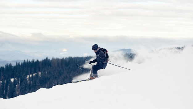 写真 雪をかぶった山頂を曲がるスキーヤー