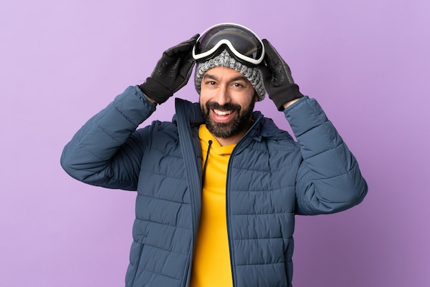 Skier man with snowboarding glasses over isolated purple wall