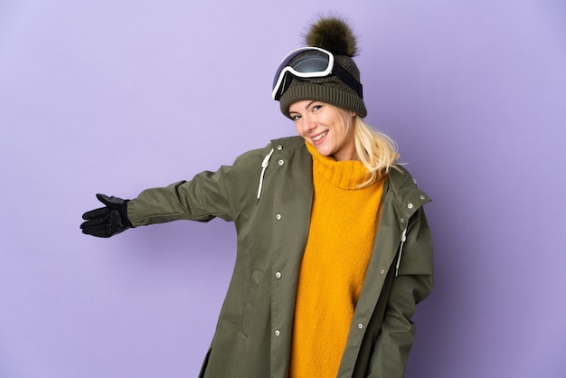 Skier Russian girl with snowboarding glasses isolated on purple background extending hands to the side for inviting to come