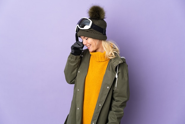 Skier Russian girl with snowboarding glasses isolated on purple background laughing