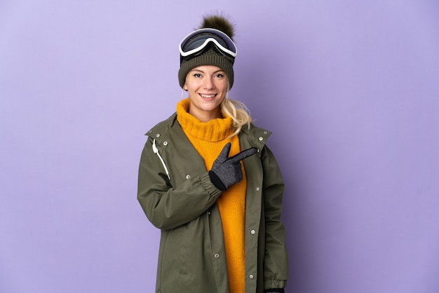 제품을 제시하기 위해 측면을 가리키는 보라색 배경에 고립 된 스노우 보드 안경 스키 러시아 소녀