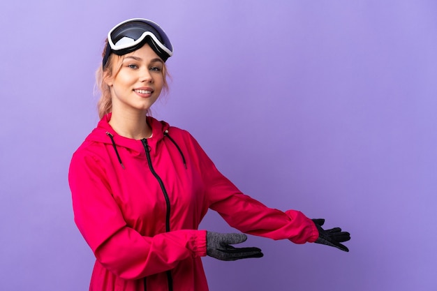 Skier teenager girl with snowboarding glasses over isolated purple  extending hands to the side for inviting to come