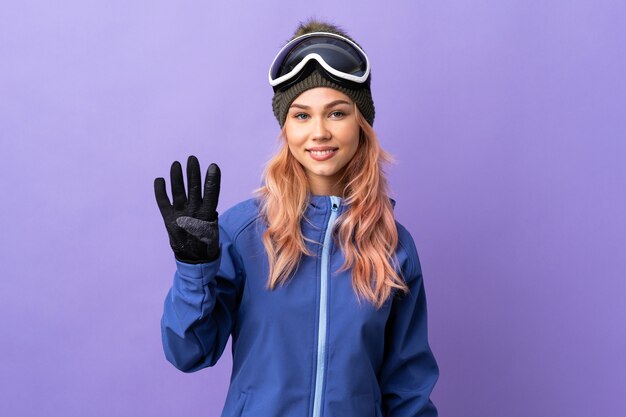 Skier teenager girl with snowboarding glasses over isolated purple wall happy and counting four with fingers