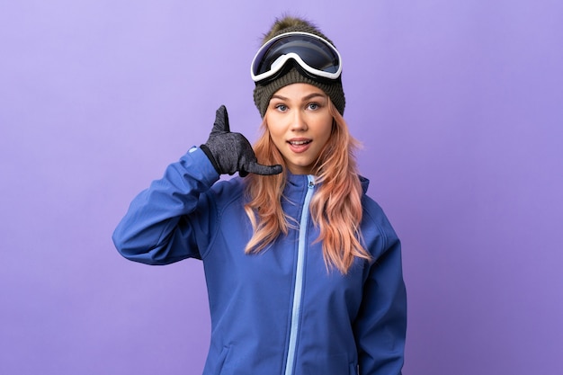 Skier teenager girl with snowboarding glasses over isolated purple wall making phone gesture. Call me back sign