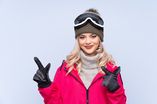 Skier teenager woman with snowboarding glasses pointing finger to the side