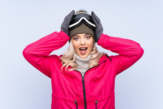 Skiër tiener meisje met snowboard bril over geïsoleerde blauw met verrassing gelaatsuitdrukking
