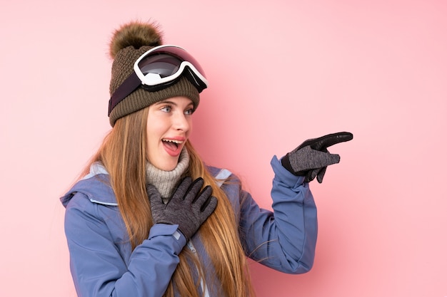 Skiër tiener meisje met snowboard bril over geïsoleerde roze wijzende vinger aan de zijkant