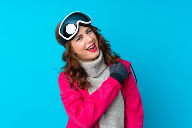 Skier woman with snowboarding glasses over isolated blue wall celebrating a victory