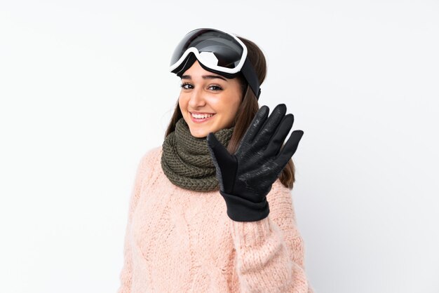 Skiërmeisje met snowboarding glazen over witte muur die met hand met gelukkige uitdrukking groeten