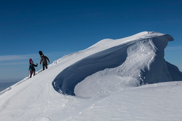 Skiers on a winter trail go around a snow cornice in the mountains