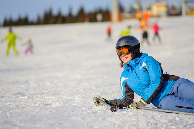 Skiërvrouw die op de sneeuw bij skitoevlucht liggen op een zonnige dag