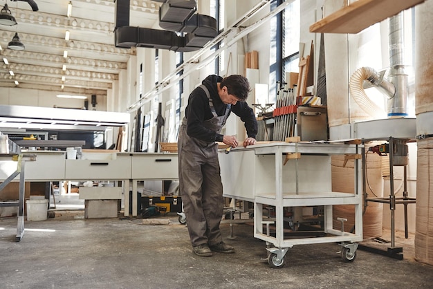 Photo skilled carpenter in grey uniform measuring a piece of wood in his woodwork workshop other machinery in the background horizontal shot fulllength