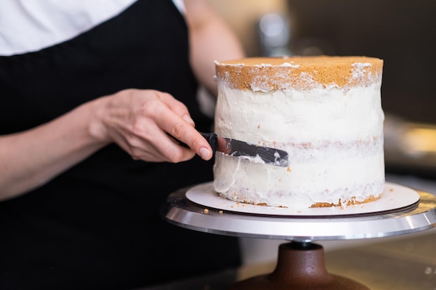 Skilled confectioner smearing sugar free white cream around baked cake with knife