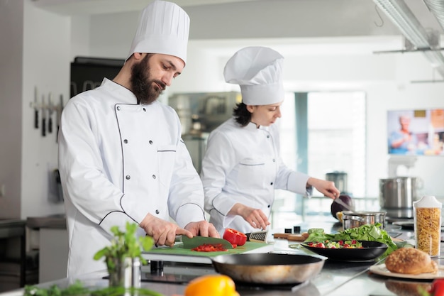 Skilled and confident head chef chopping organic and fresh red bell pepper while preparing garnish. Food industry worker cooking delicious gourmet dish for dinner service at restaurant.