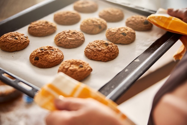 Skilled cook cautiously carrying tray with hot cookies