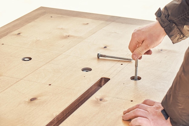 Skilled craftsman assembles large wooden dining table turning bolts with hand outdoors