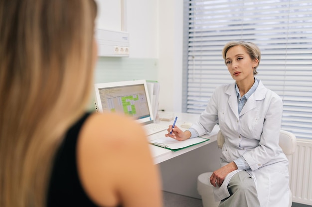 Skilled female doctor in white coat listening of unrecognizable woman patient tell about chronic