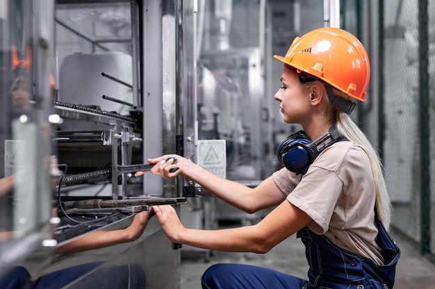 Skilled female repairing broken equipment in factory using\
wrench, in workwear