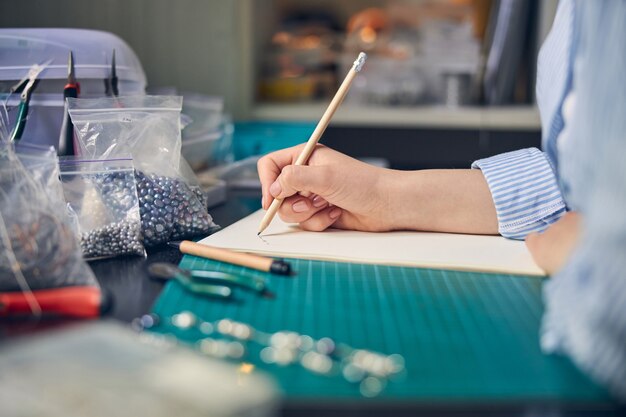 Skilled jewel employee using a pencil and creating a necklace draft on paper