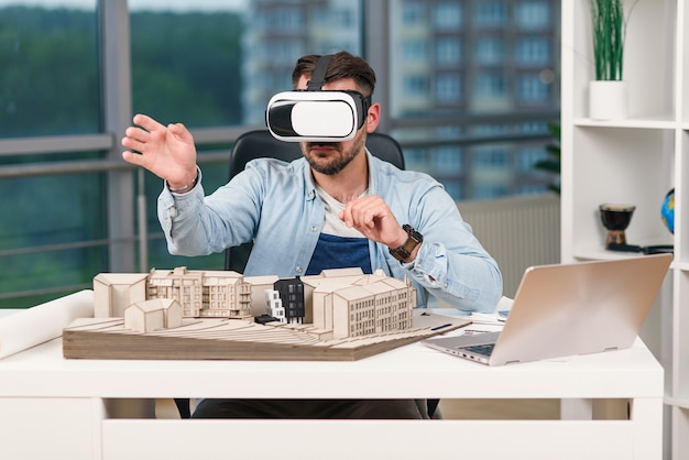 Skilled male architect reviewing an architectural project with augmented reality glasses in design bureau