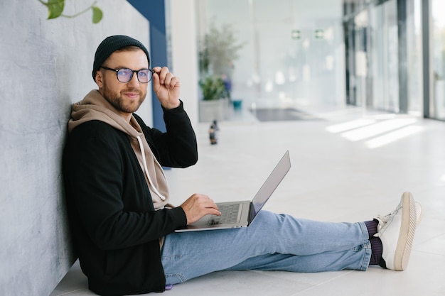 Skilled male it developer looking at camera coding on modern laptop computer working on freelance in office interior portrait of cheerful hipster guy using netbook for e learning