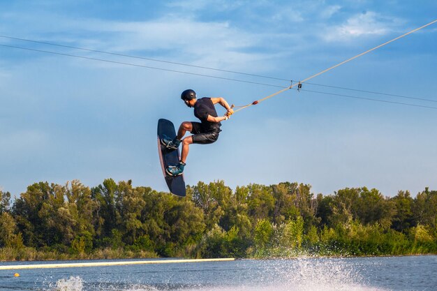 Skilled male wakeboarder jumping with backside rotation over water holding rope in hand