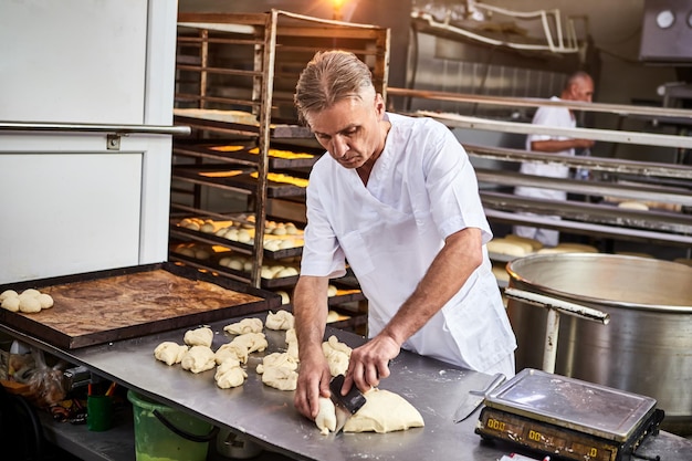 Skilled man baker dividing raw dough into equal portions and weights them Process of making bread in bakery