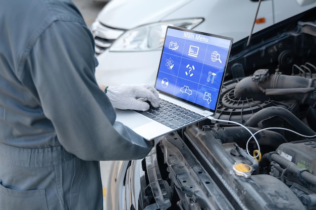 Skilled mechanic using a laptop computer to check collect information during work a car engine