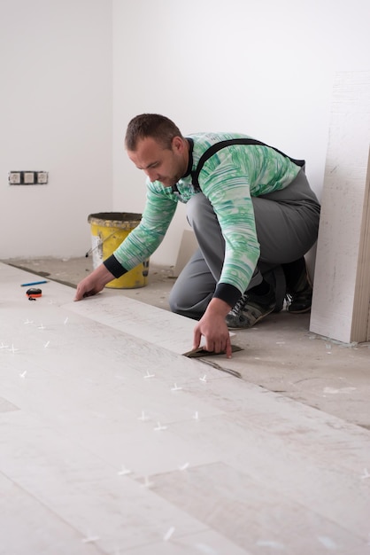 skilled worker installing the ceramic wood effect tiles on the floor Worker making laminate flooring on the construction site of the new apartment